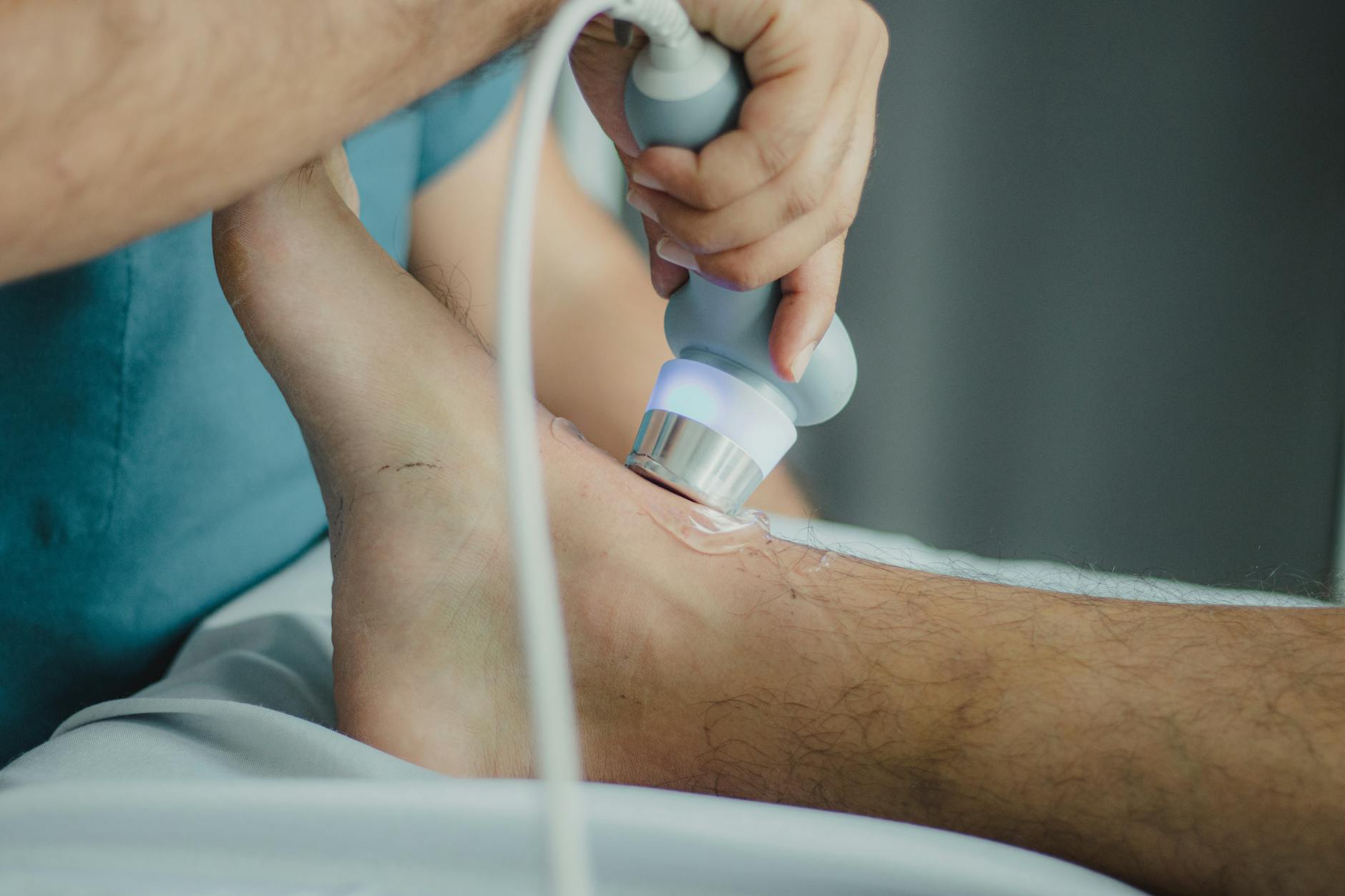Fizjoterapeuta wykonuje zabieg USG na łydce pacjenta