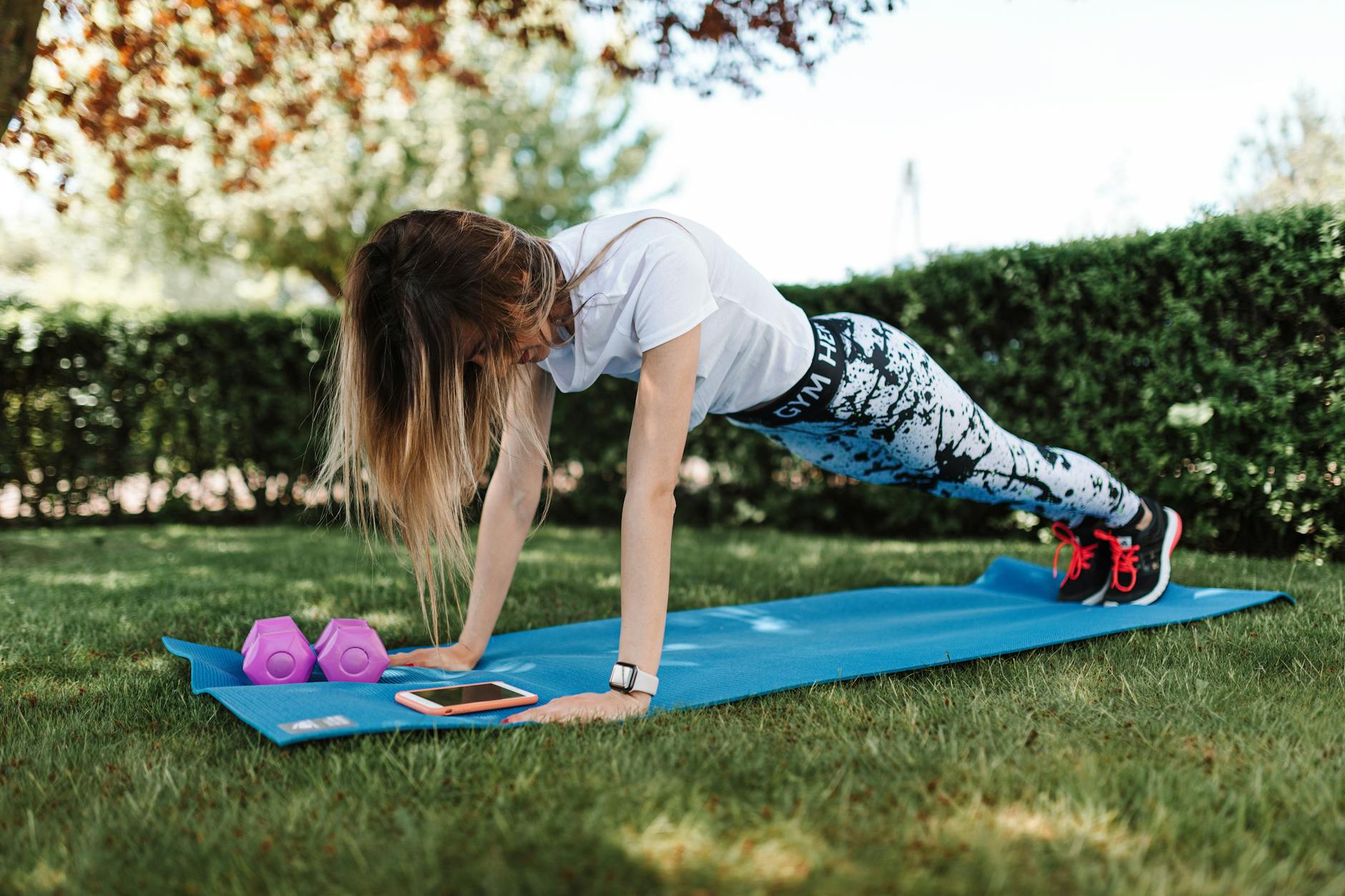 Kobieta robi pompki na macie z hantlami i smartfonem obok