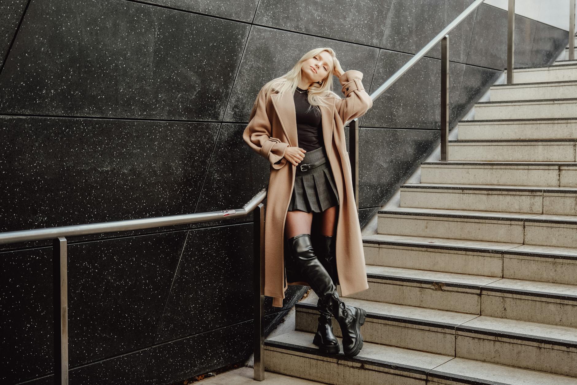 Kobieta w płaszczu i kozakach stoi na miejskich schodach