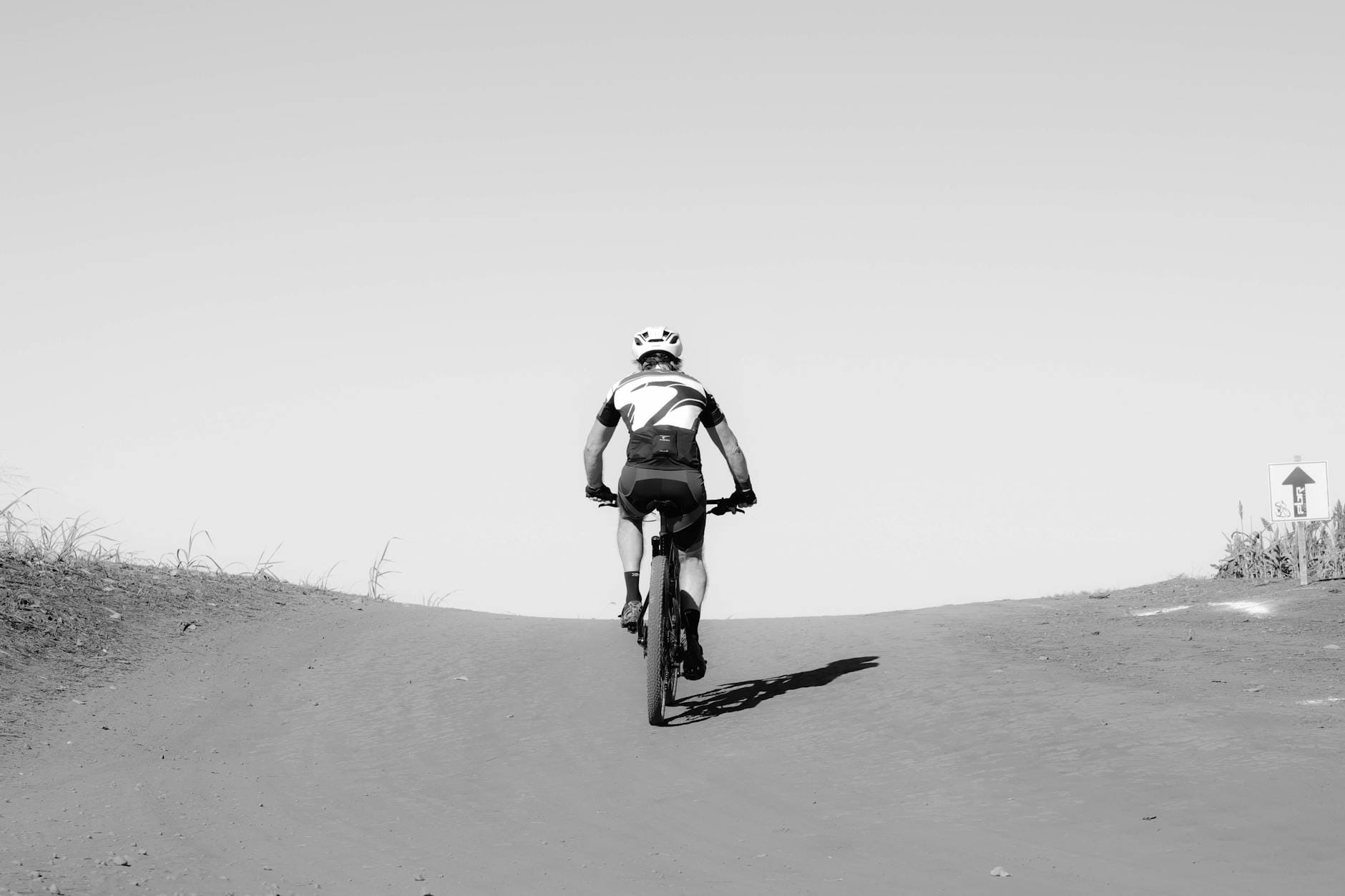 Kolarz podjeżdża rowerem pod górę po leśnej, piaszczystej ścieżce