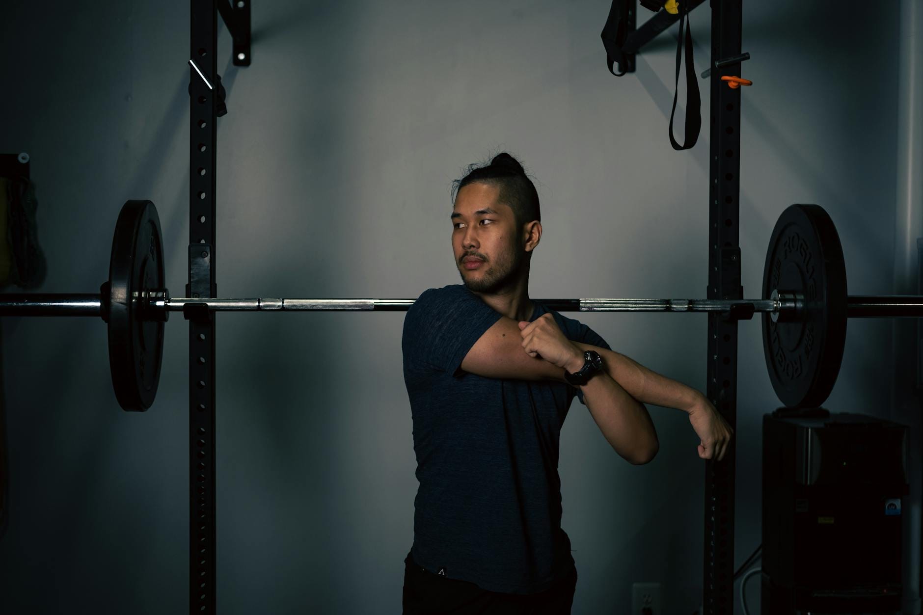 Mężczyzna rozciąga barki przy sztandze w domowej siłowni