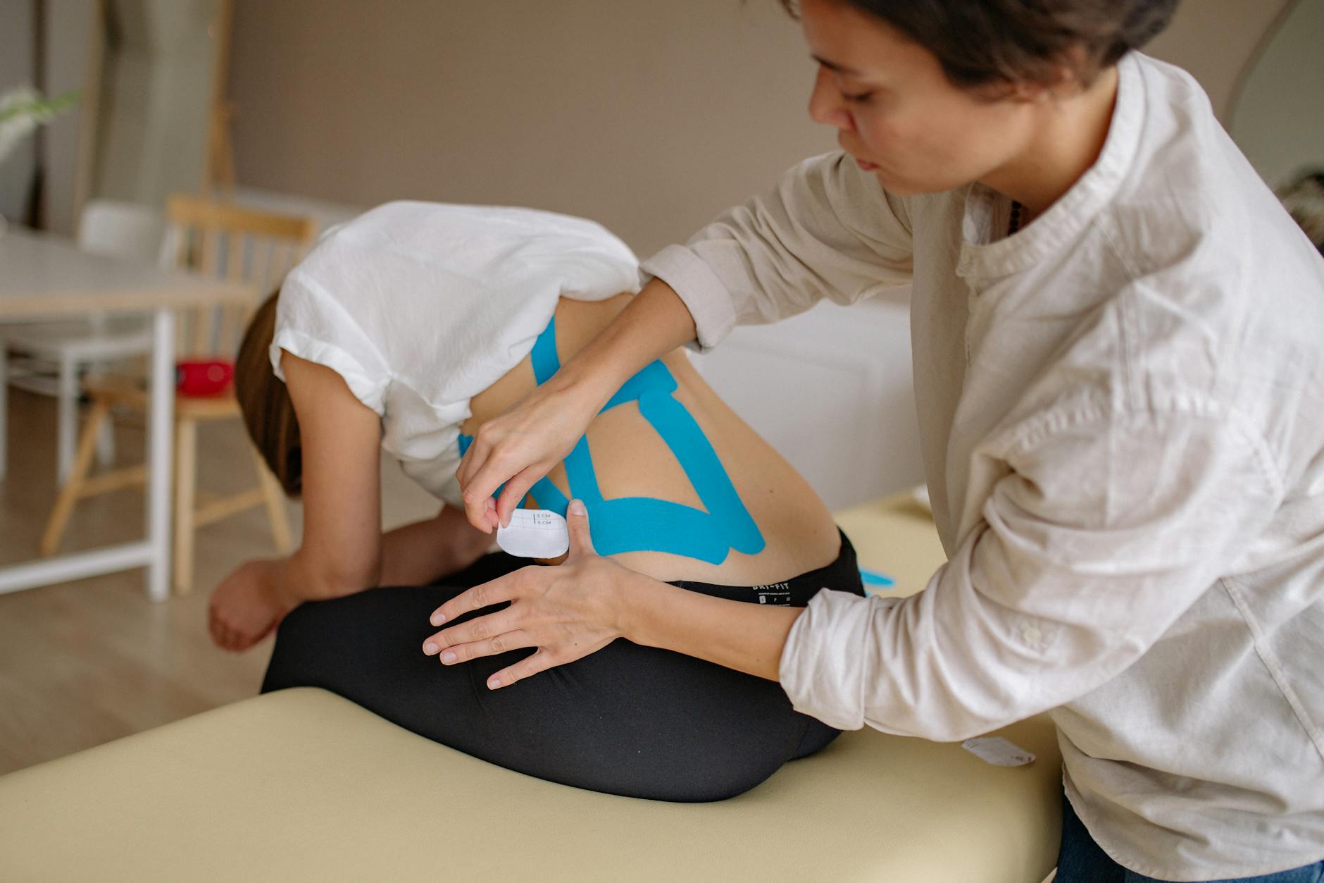 Terapeuta nakleja niebieskie taśmy kinesiotaping na plecach pacjenta