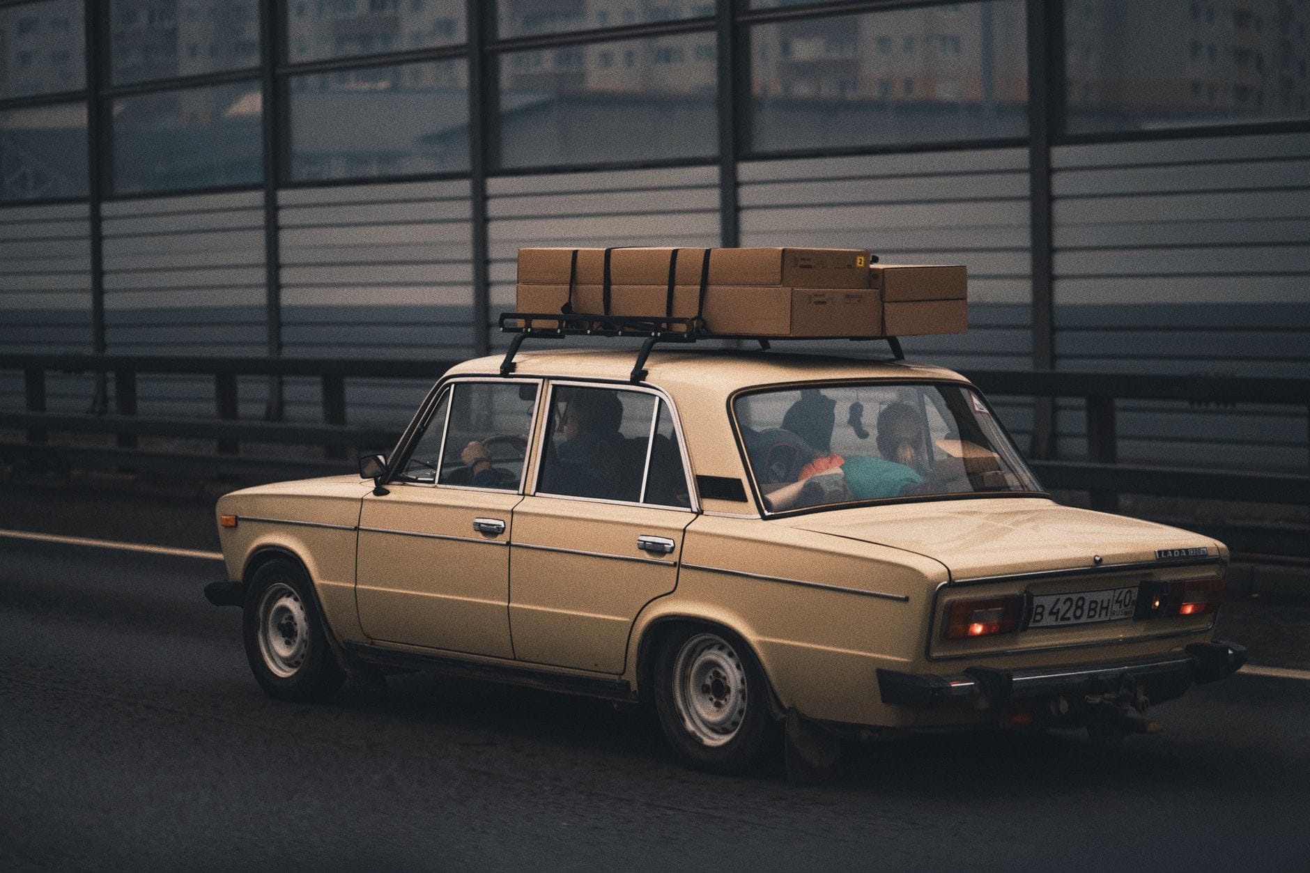 Beżowy sedan z bagażem na dachu jedzie autostradą obok miasta