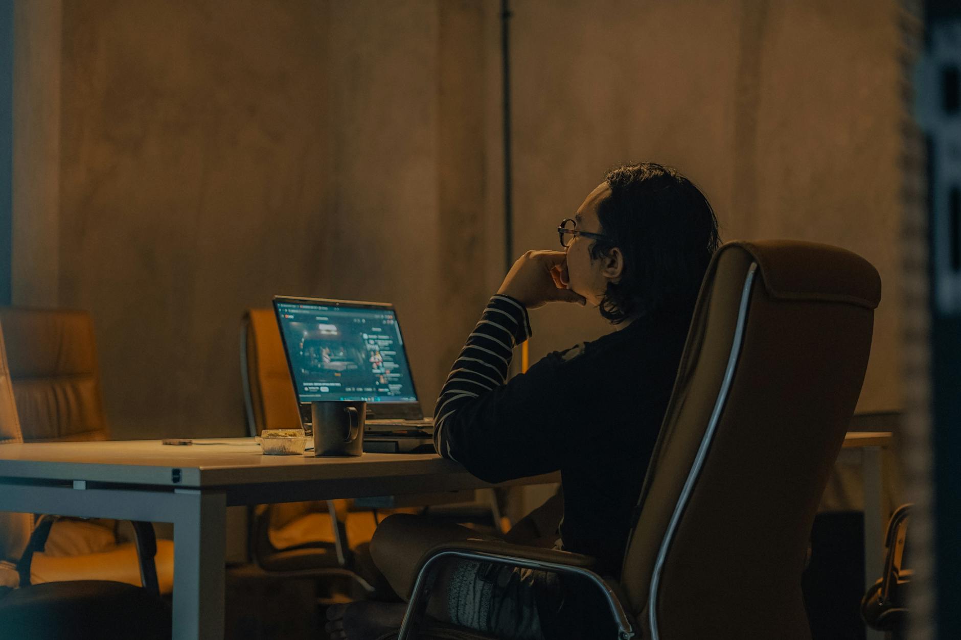 Mężczyzna pracuje przy laptopie przy biurku w słabo oświetlonym biurze Mężczyzna pracuje przy laptopie przy biurku w słabo oświetlonym biurze